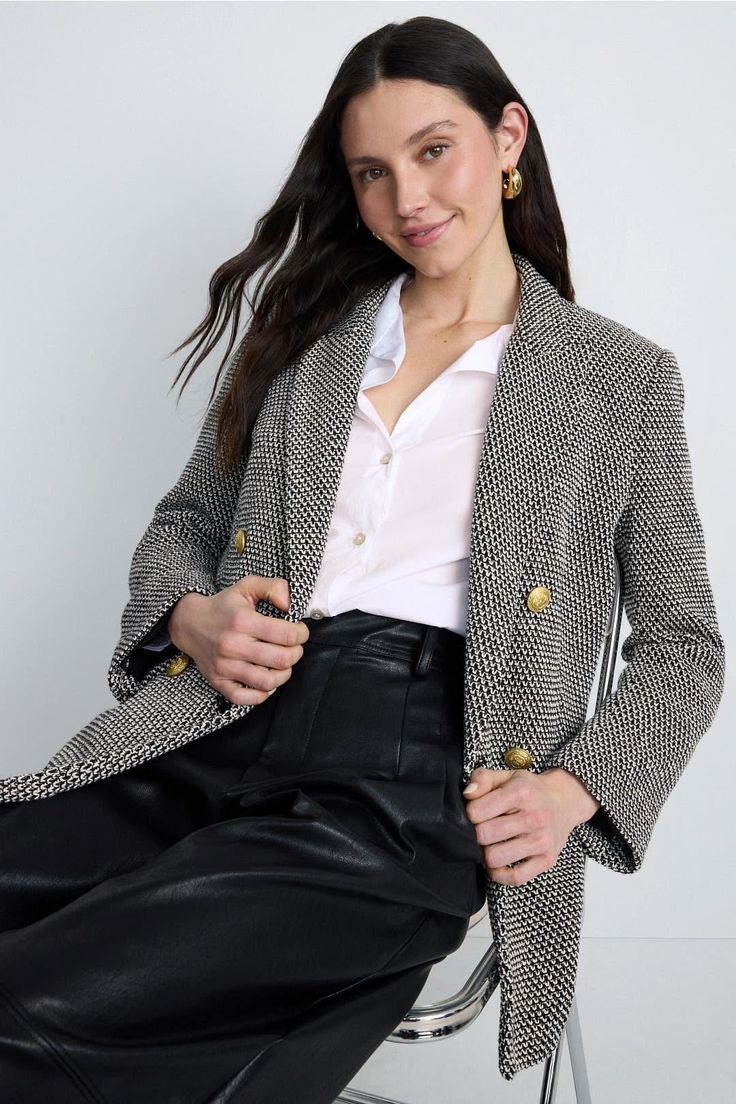Woman with long dark hair wearing a blazer and black pants, sitting indoors