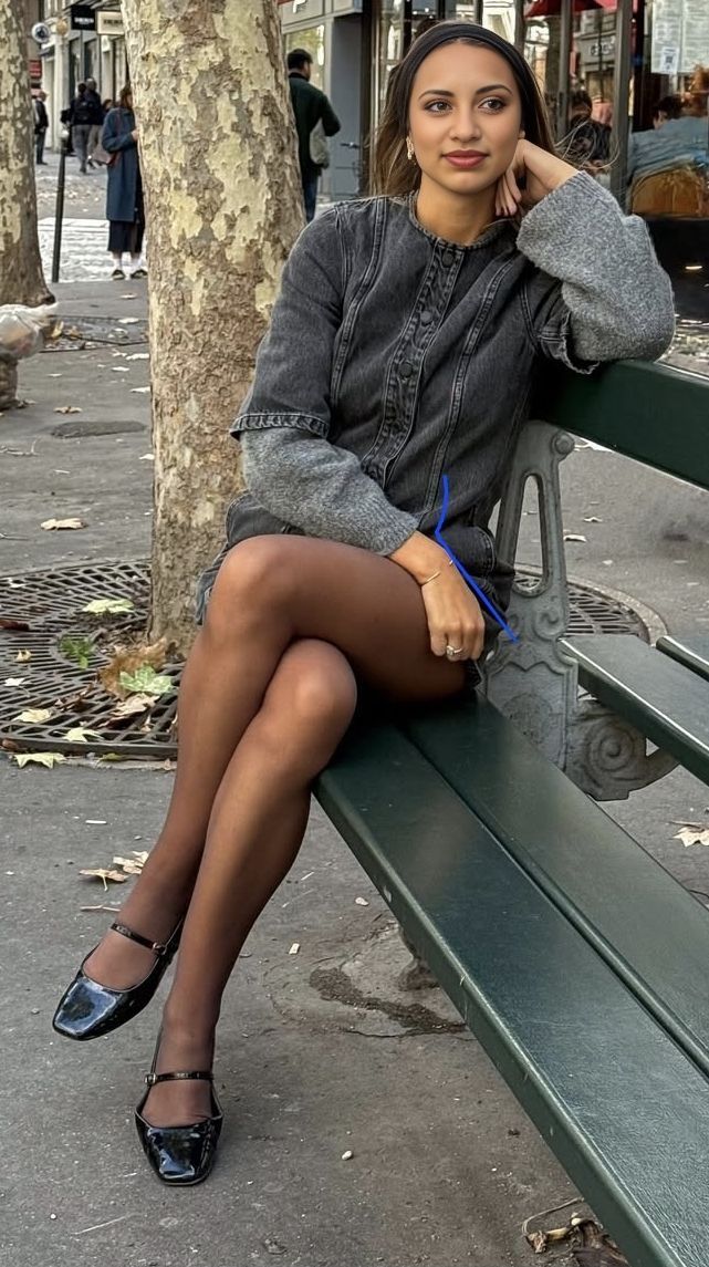 Woman in a denim dress and tights sitting on a park bench outdoors