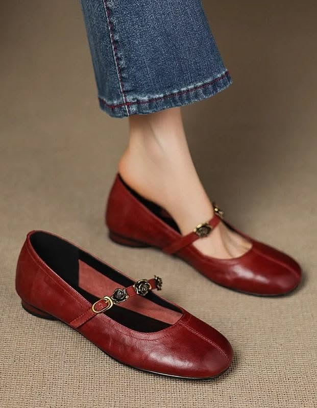 Close up of a person wearing red mary jane flats with rose buckles and denim jeans