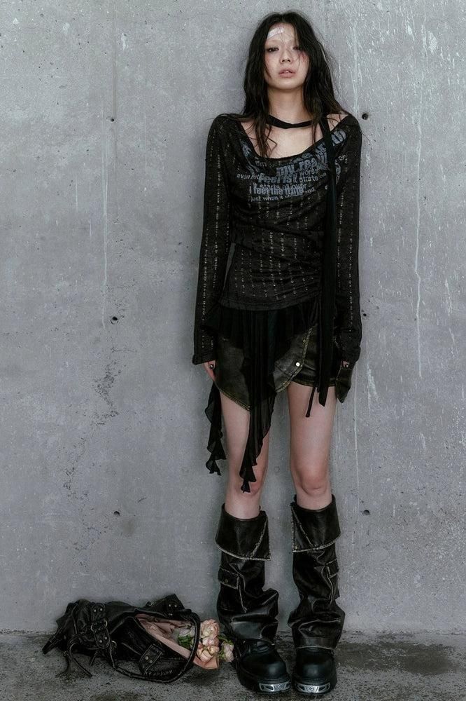 Woman in dark, distressed clothing and boots against a concrete wall
