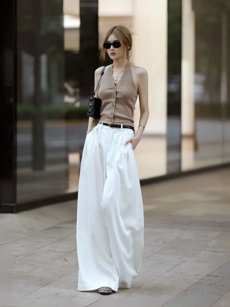 Woman in a halter top and wide leg pants with sunglasses and a shoulder bag