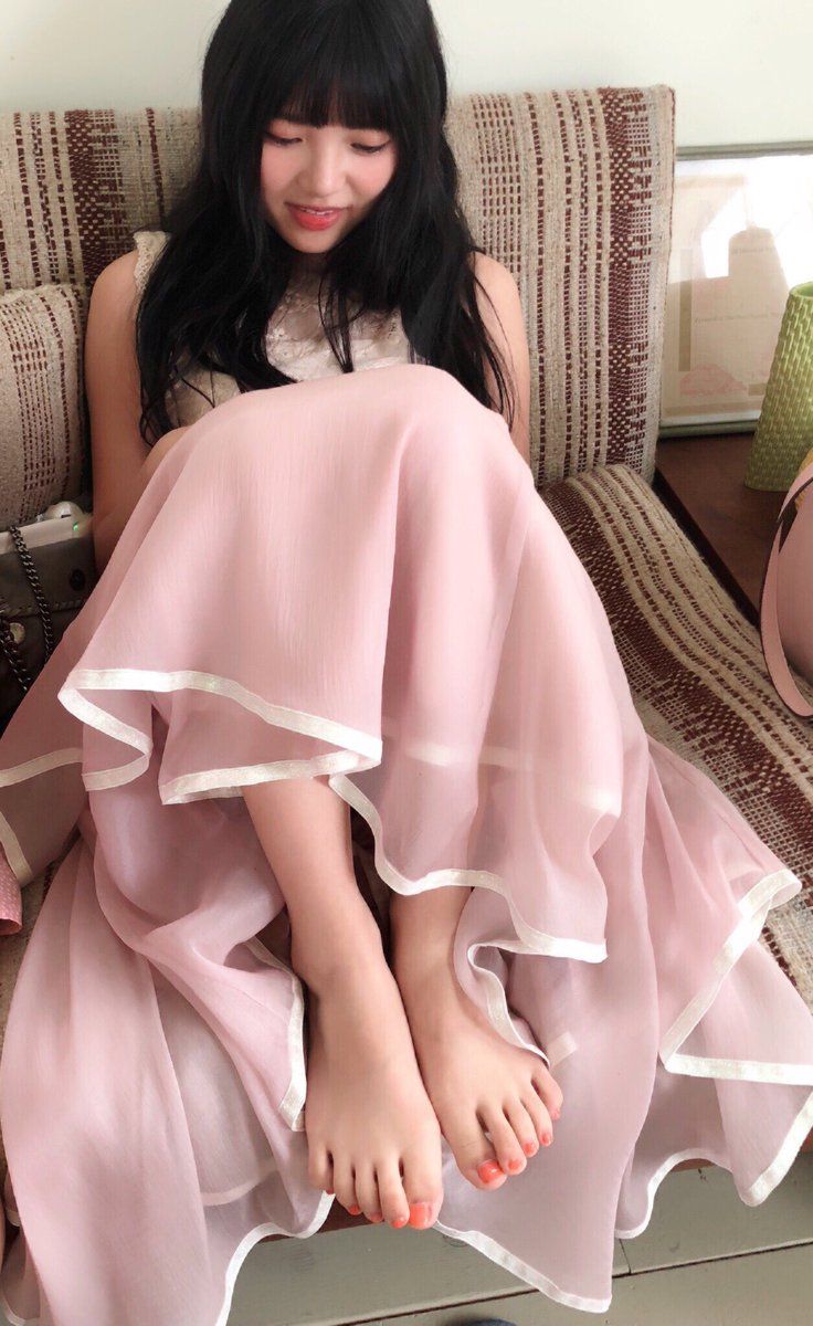 Woman with long black hair in a pink dress sitting indoors with bare feet