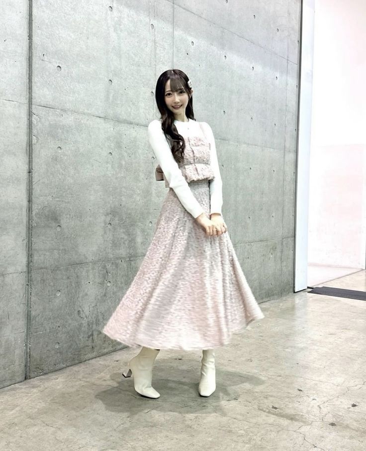 Woman in a pink dress and white boots smiling in front of a concrete wall