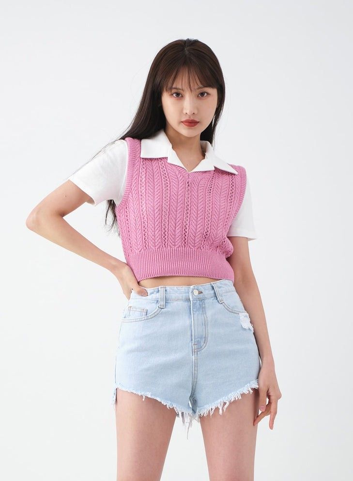 Woman in a pink knit vest and denim shorts posing in a studio