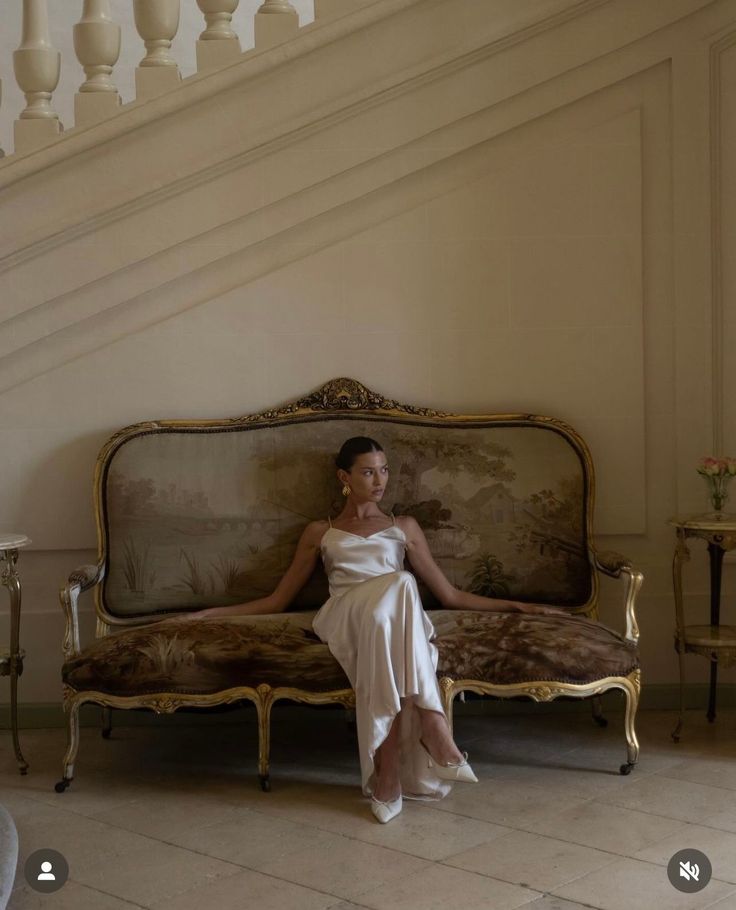 Woman in a satin dress sitting on an ornate sofa indoors