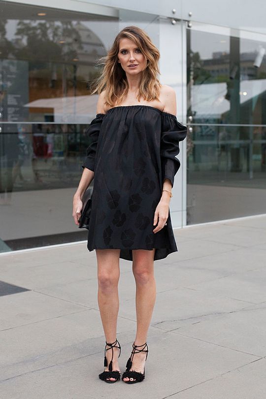 Woman in a black off-shoulder dress and high heels standing outdoors