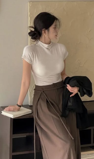 Woman in a white t-shirt and brown pants with hair bun indoors