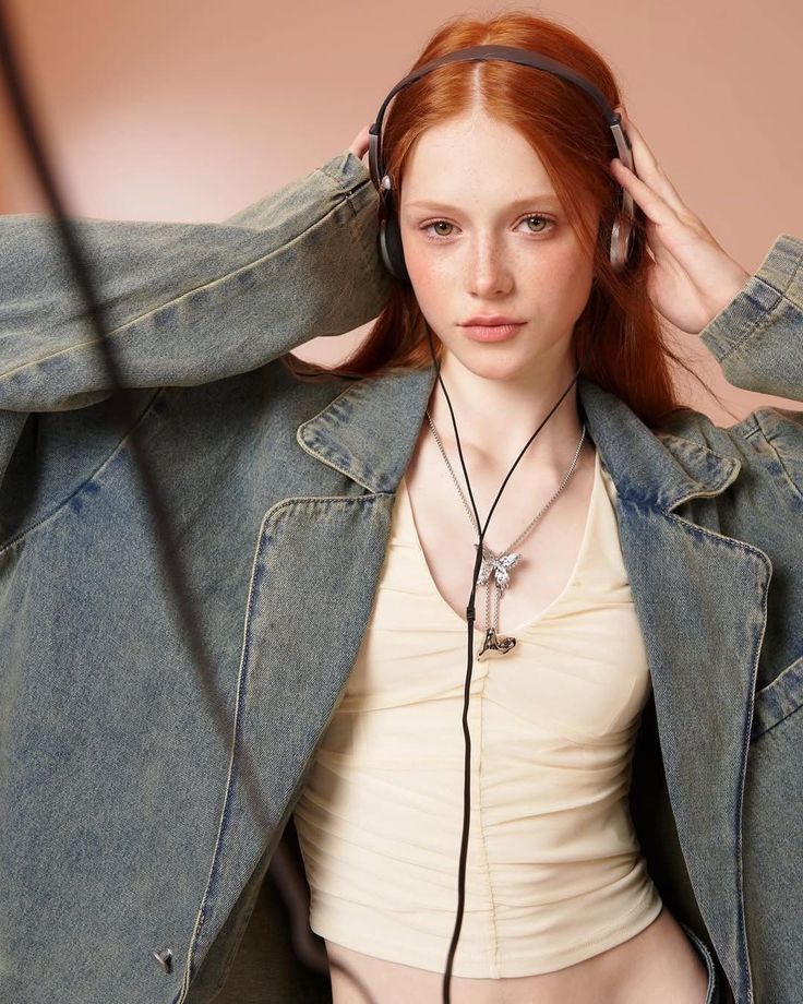 Woman with red hair and freckles wearing headphones and a denim jacket