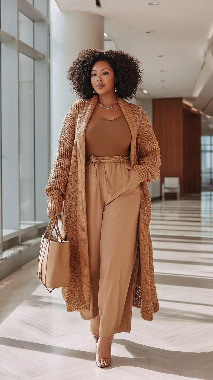 Woman with curly hair wearing a long cardigan and wide leg pants indoors
