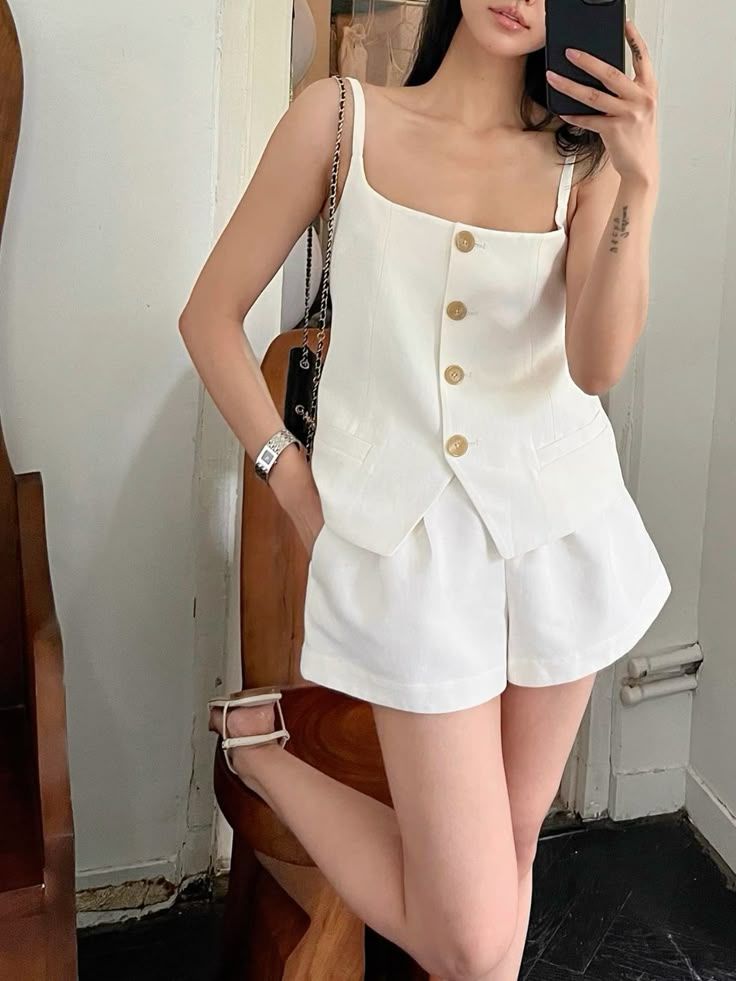 Woman in a white top and shorts taking a mirror selfie indoors