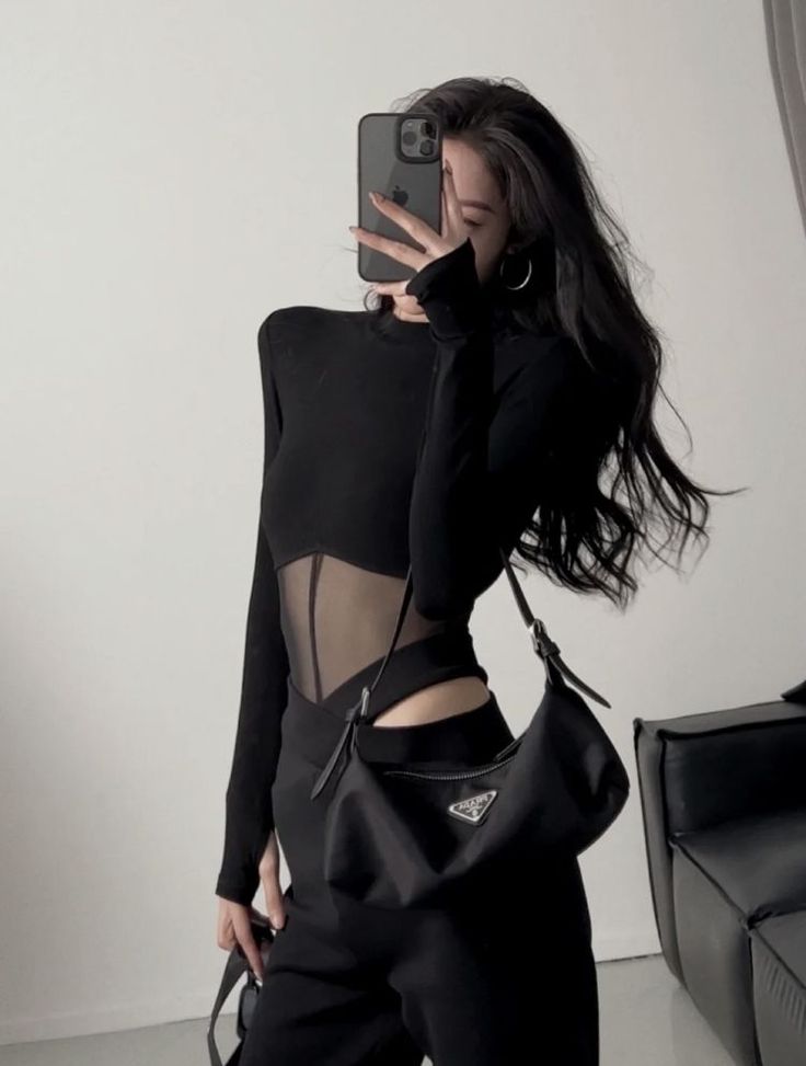 Woman in a black top with sheer panels taking a mirror selfie