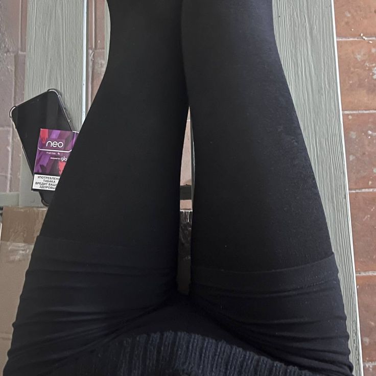 Person wearing black leggings with a phone and cigarette pack nearby