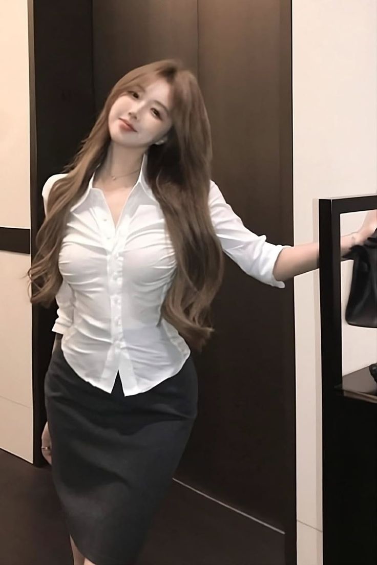 Woman with long brown hair wearing a white shirt and pencil skirt indoors