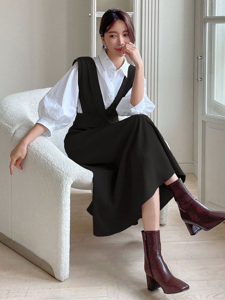 Woman in a black dress and white shirt sitting on a chair indoors