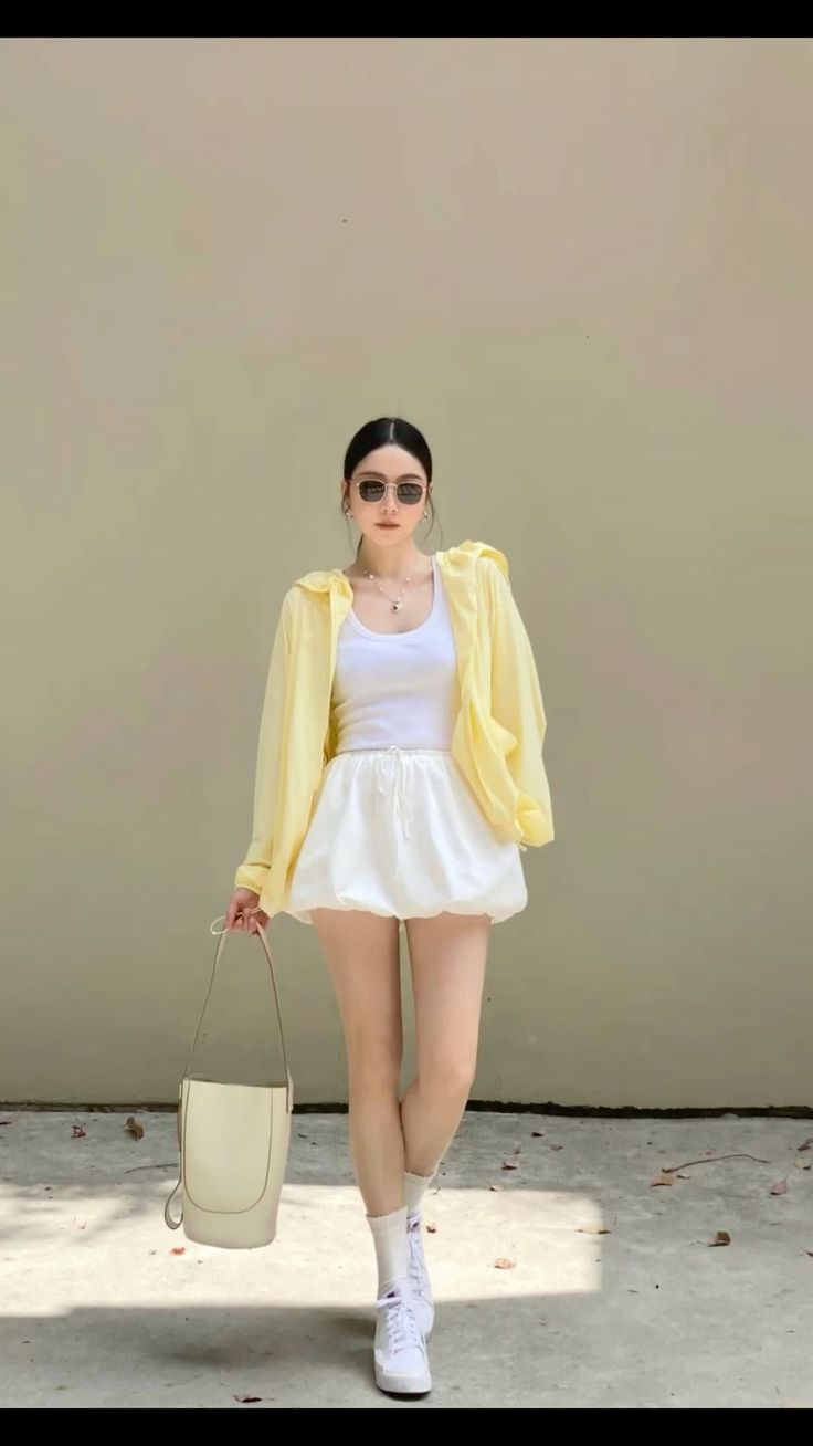 Woman in a yellow jacket, white tank top, and white shorts holding a bag