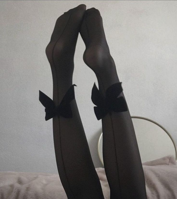 Legs in black stockings with bows, raised against a light wall