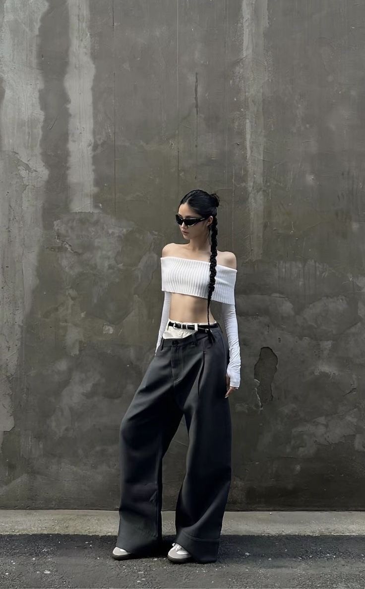 Woman in an off-shoulder crop top and wide-leg pants against a concrete wall