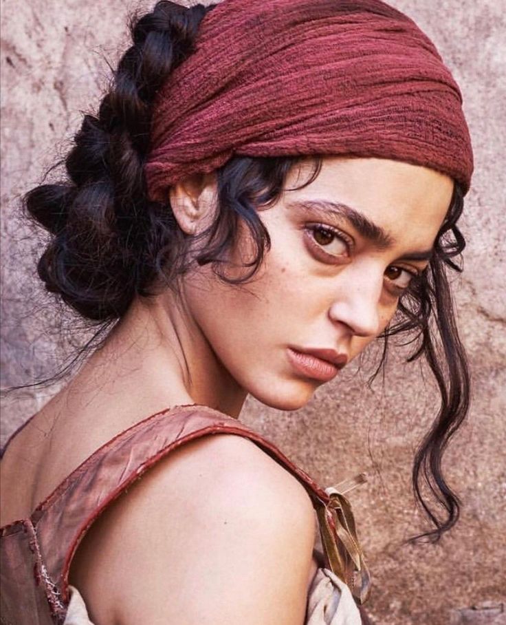 Woman with a red headscarf and dark braided hair looking over her shoulder