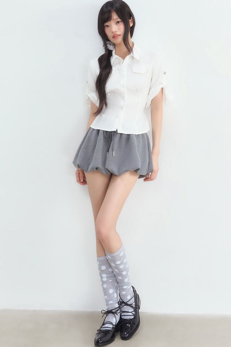 Woman with long black hair wearing a white shirt and grey skirt with polka dot socks