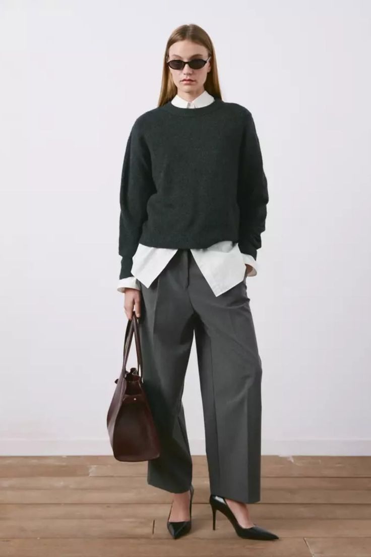 Woman in a dark sweater, white shirt, and wide leg pants holding a handbag
