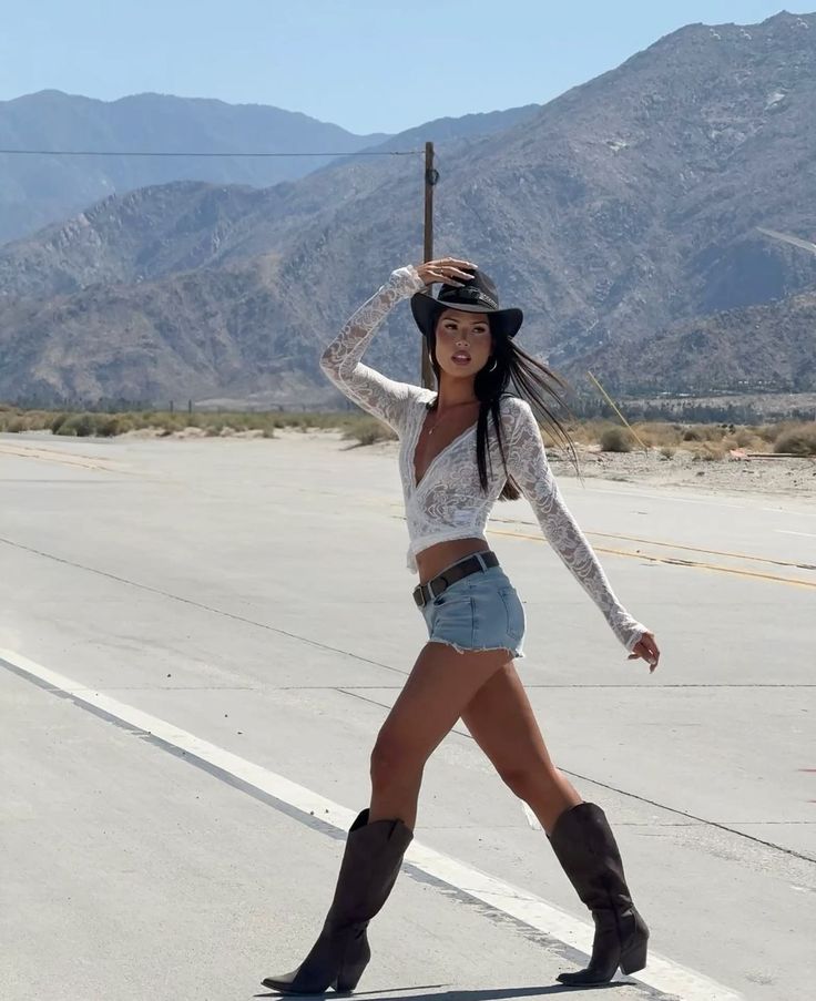 Woman in a cowboy hat, denim shorts, and boots on a desert road