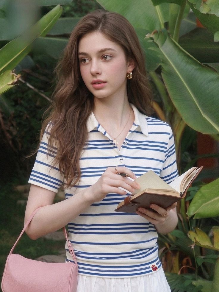 Woman with long hair wearing a striped shirt, holding a book outdoors