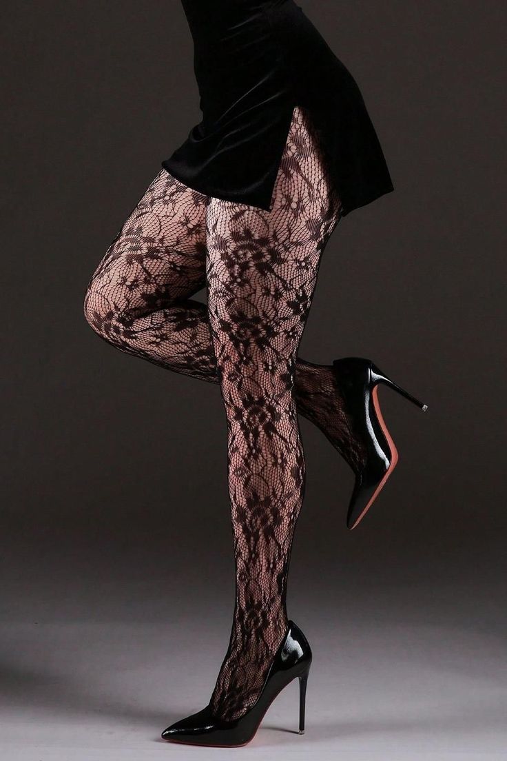 Woman in a black dress, lace tights, and high heels posing in a studio