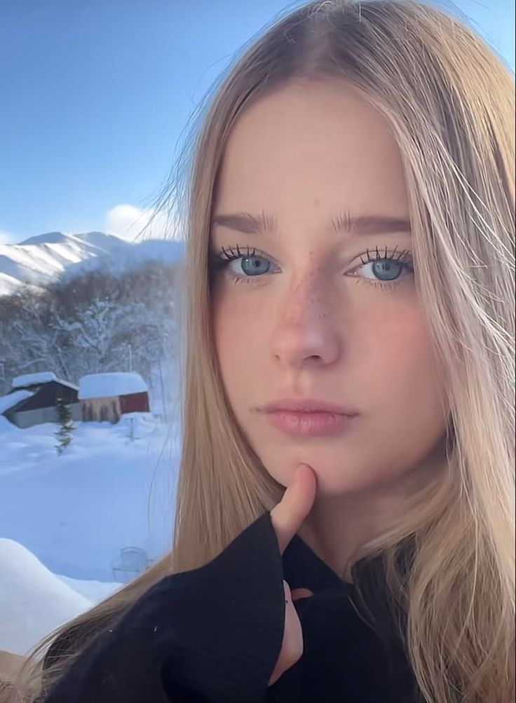 Young woman with blonde hair and blue eyes in a snowy mountain landscape