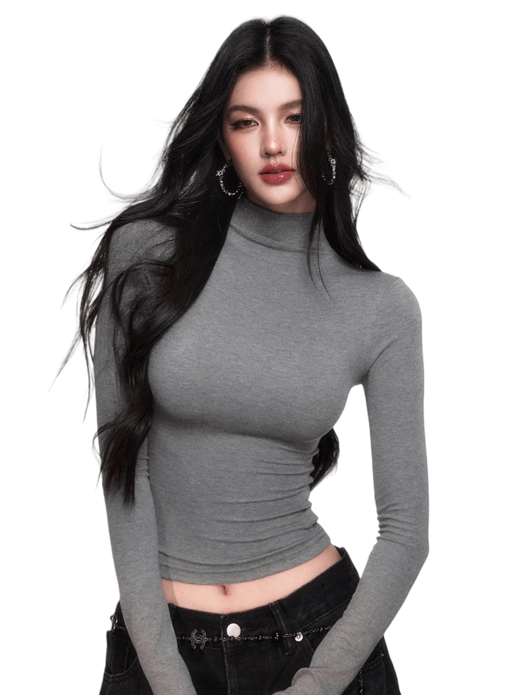 Woman with long black hair wearing a gray turtleneck cropped top and black jeans