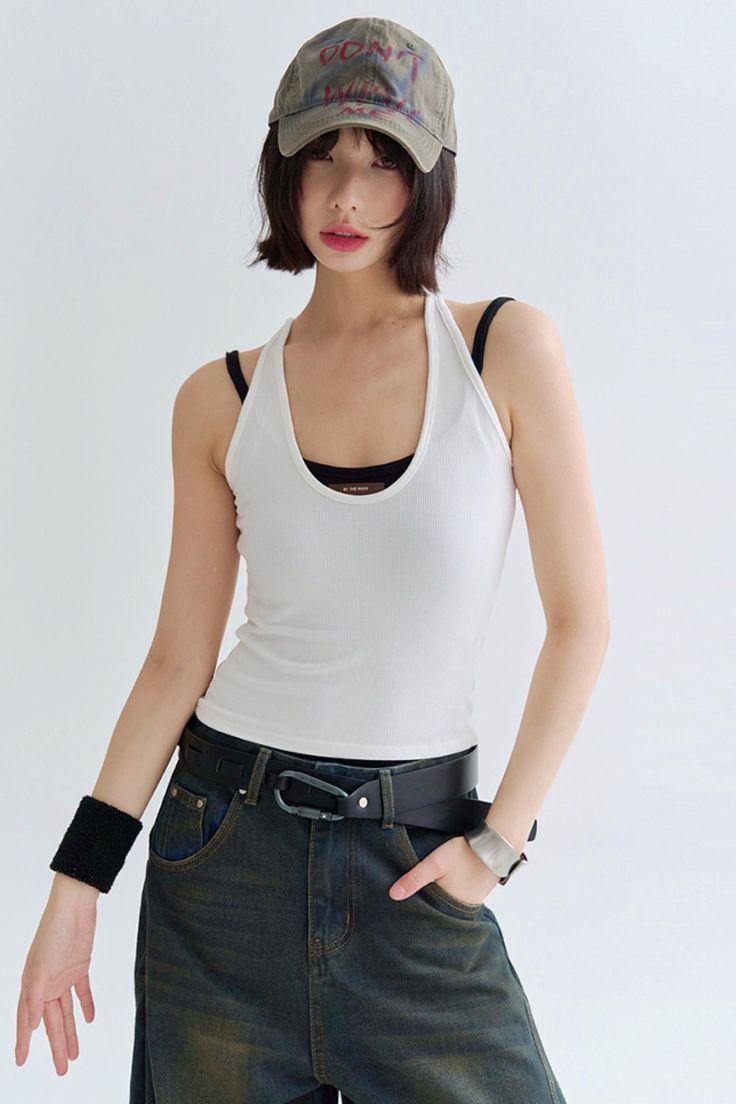 Woman with short hair and a baseball cap wearing a white tank top and jeans