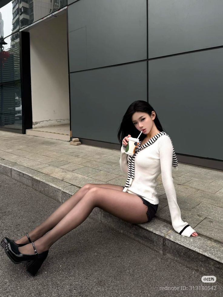 Woman with long black hair wearing a white cardigan and black shorts, sitting outdoors
