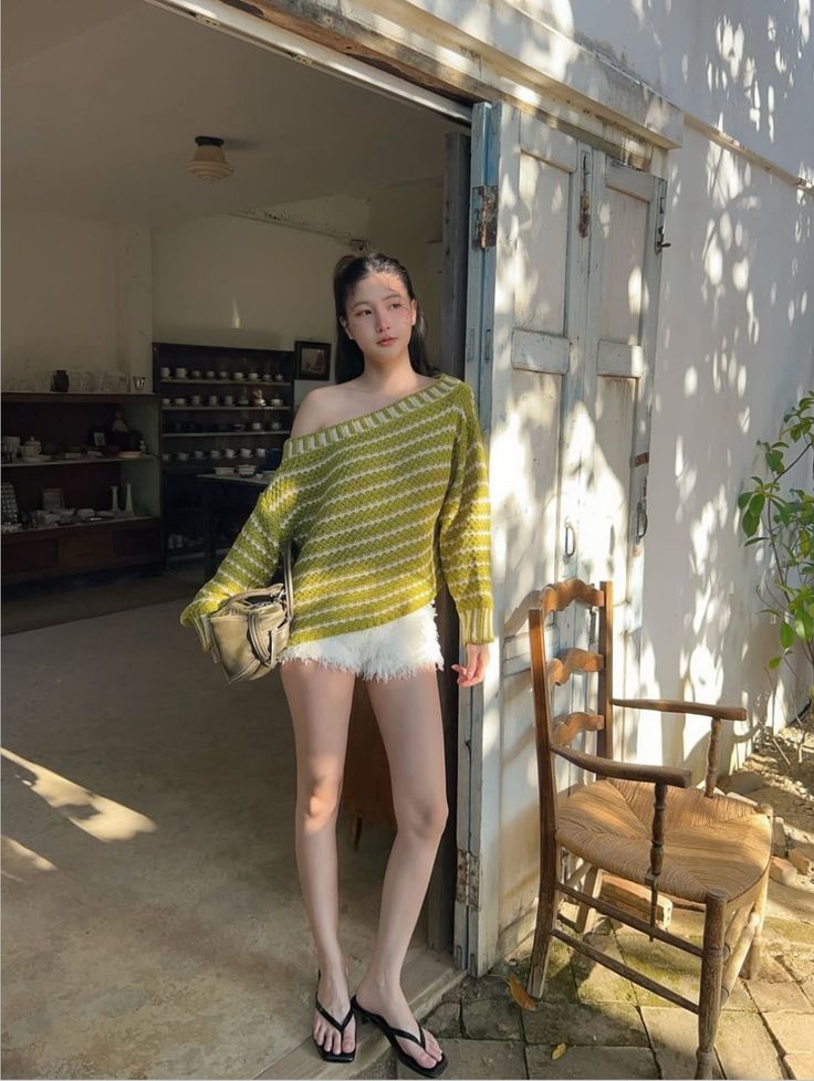 Woman in an off-shoulder sweater and white shorts standing outdoors