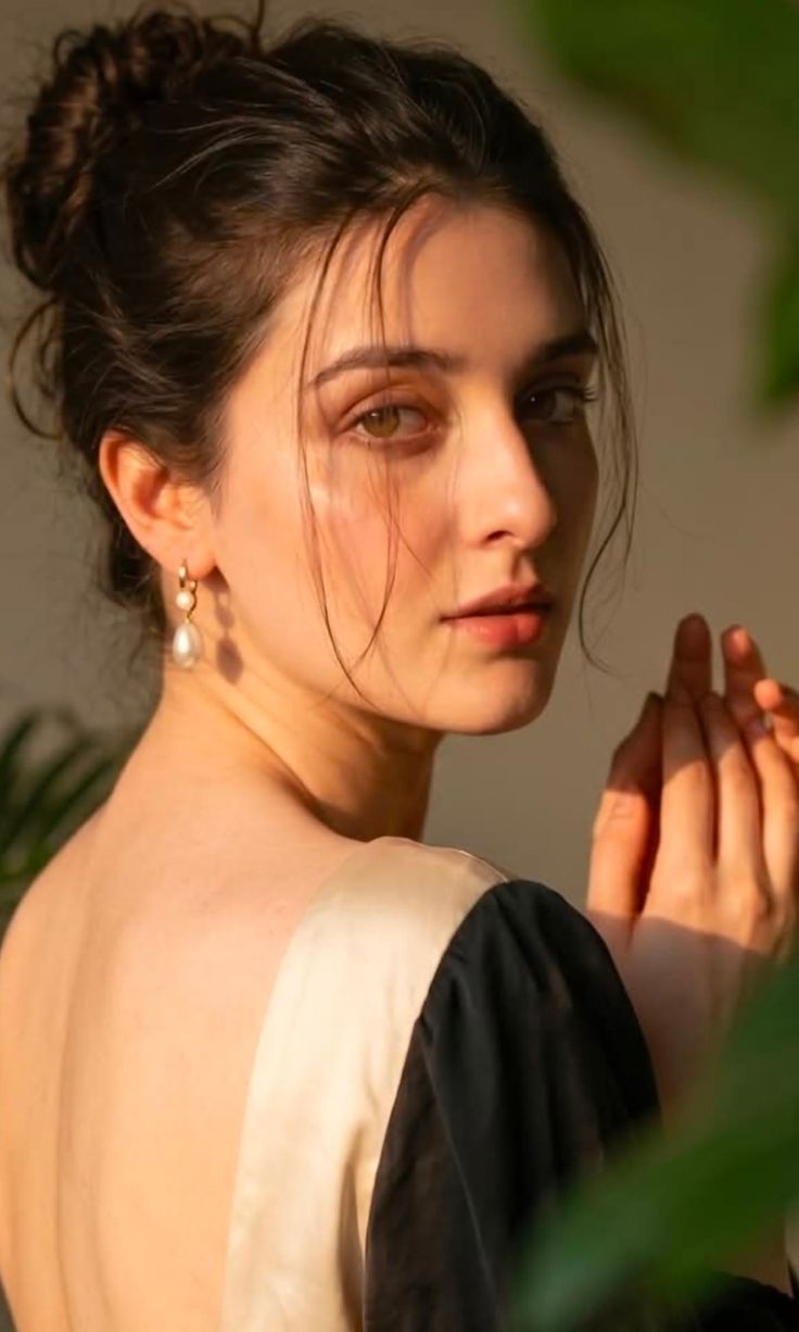 Woman with dark hair and pearl earrings, looking over her shoulder
