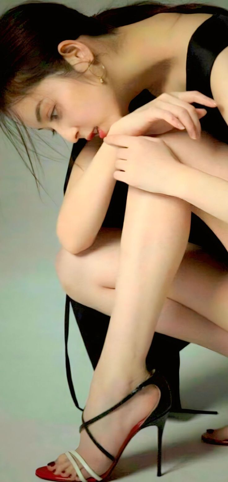 Woman in a black dress and high heels crouching indoors