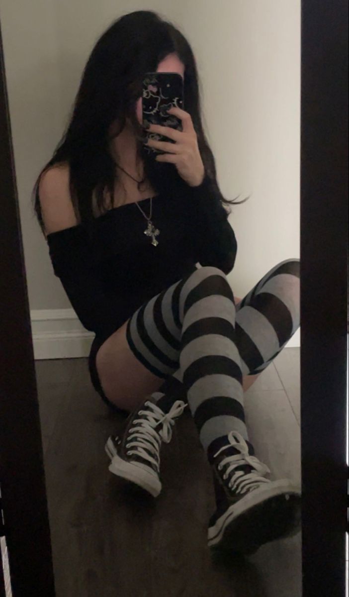 Person with long black hair taking a mirror selfie, wearing striped socks and an off-shoulder top