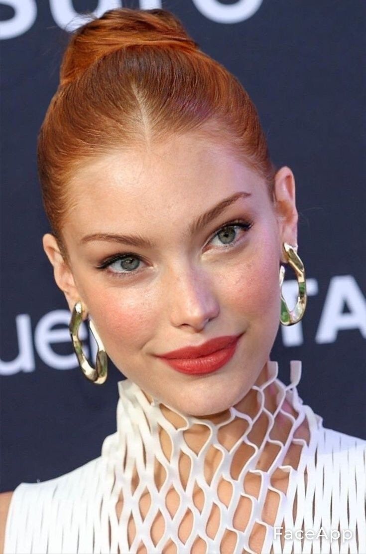 Woman with red hair in a bun wearing a white high-neck dress and gold earrings