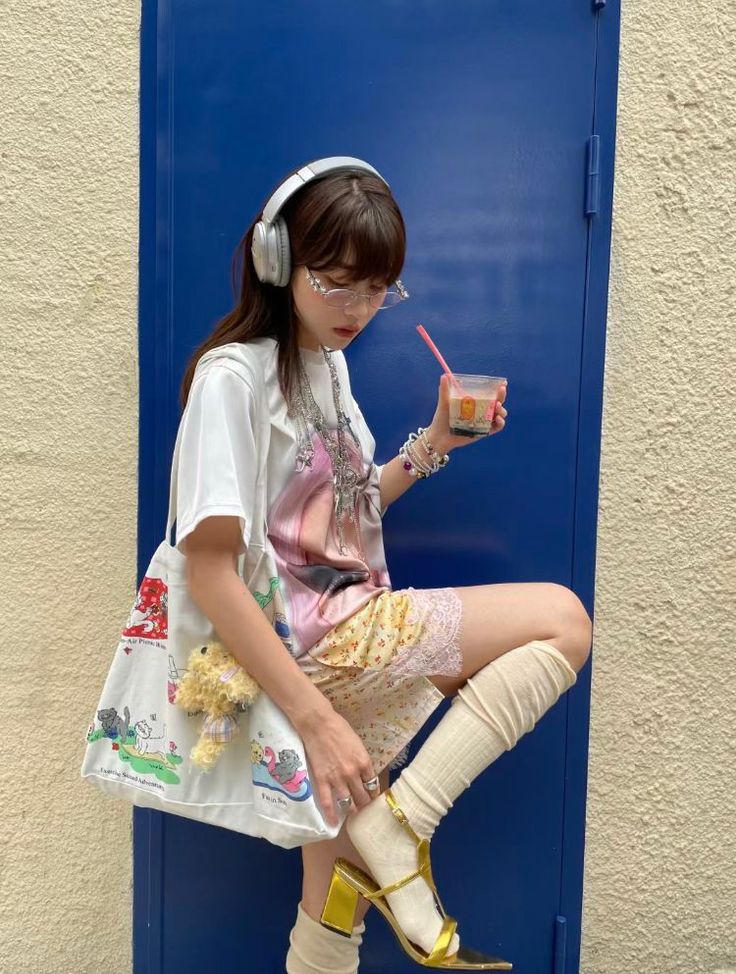 Woman with headphones and glasses holding a drink, wearing lace shorts and gold heels