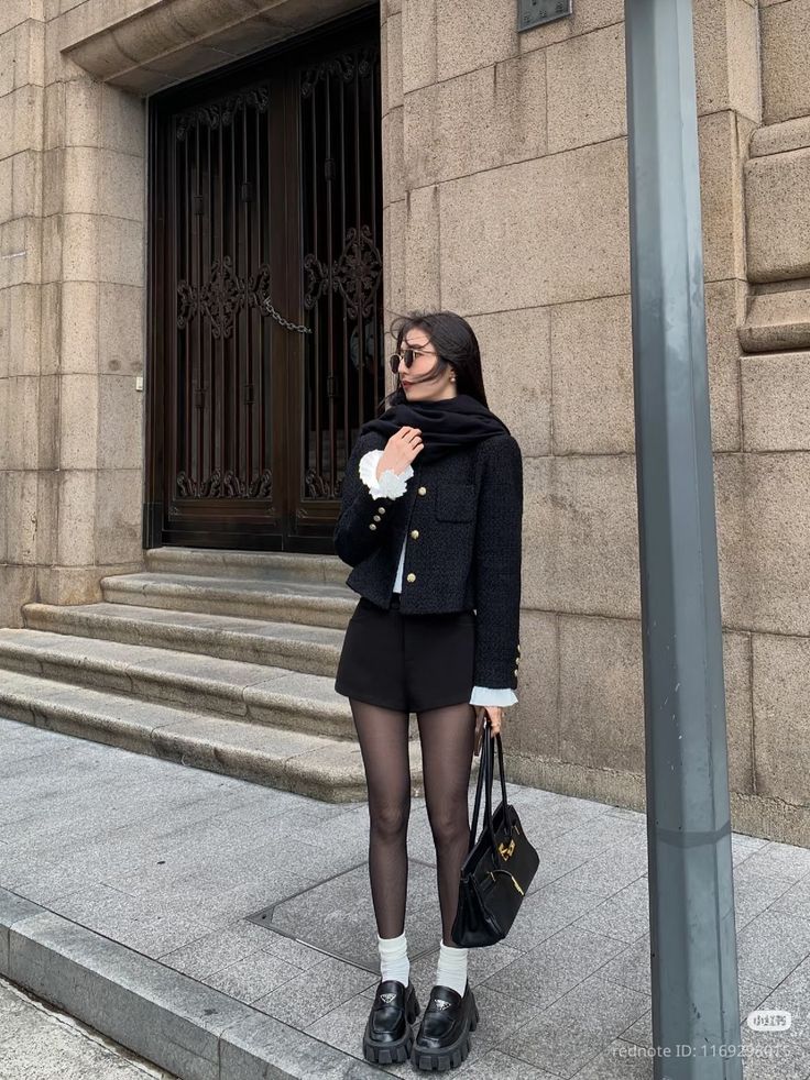 Woman in a black jacket, shorts, and tights standing on a city street