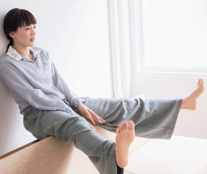 Woman in pajamas sitting indoors with bare feet, looking out a window
