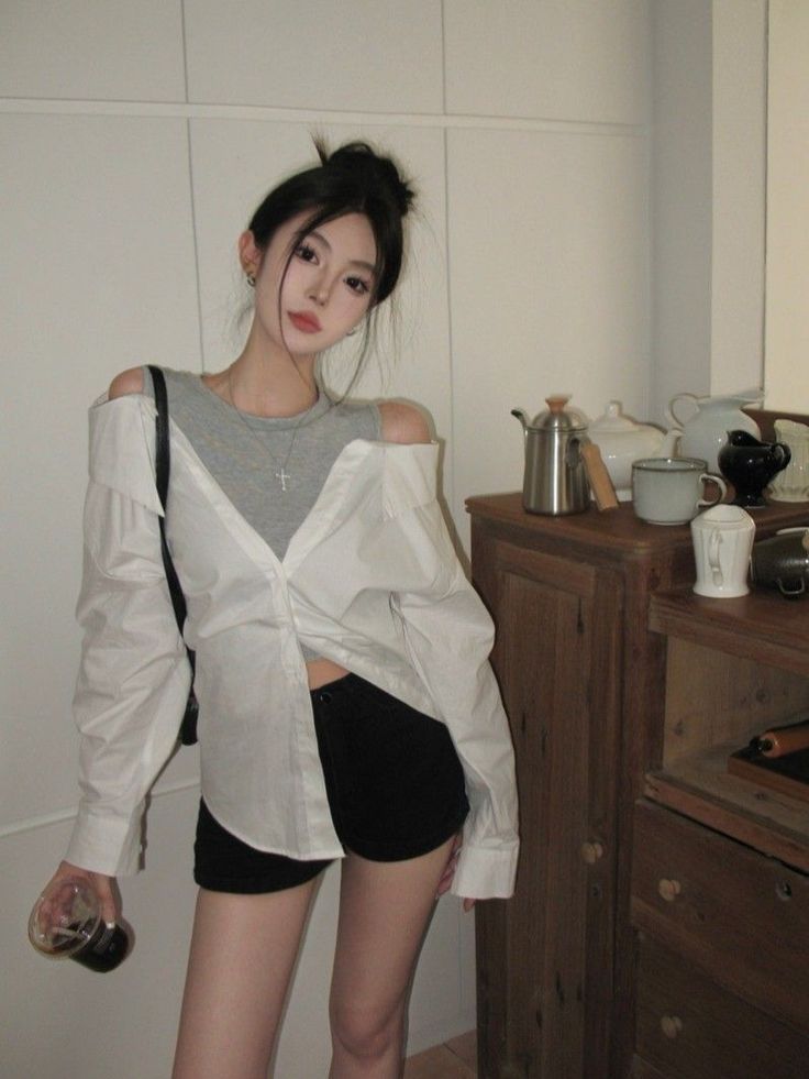 Woman with a messy bun wearing an off-shoulder shirt and black shorts indoors
