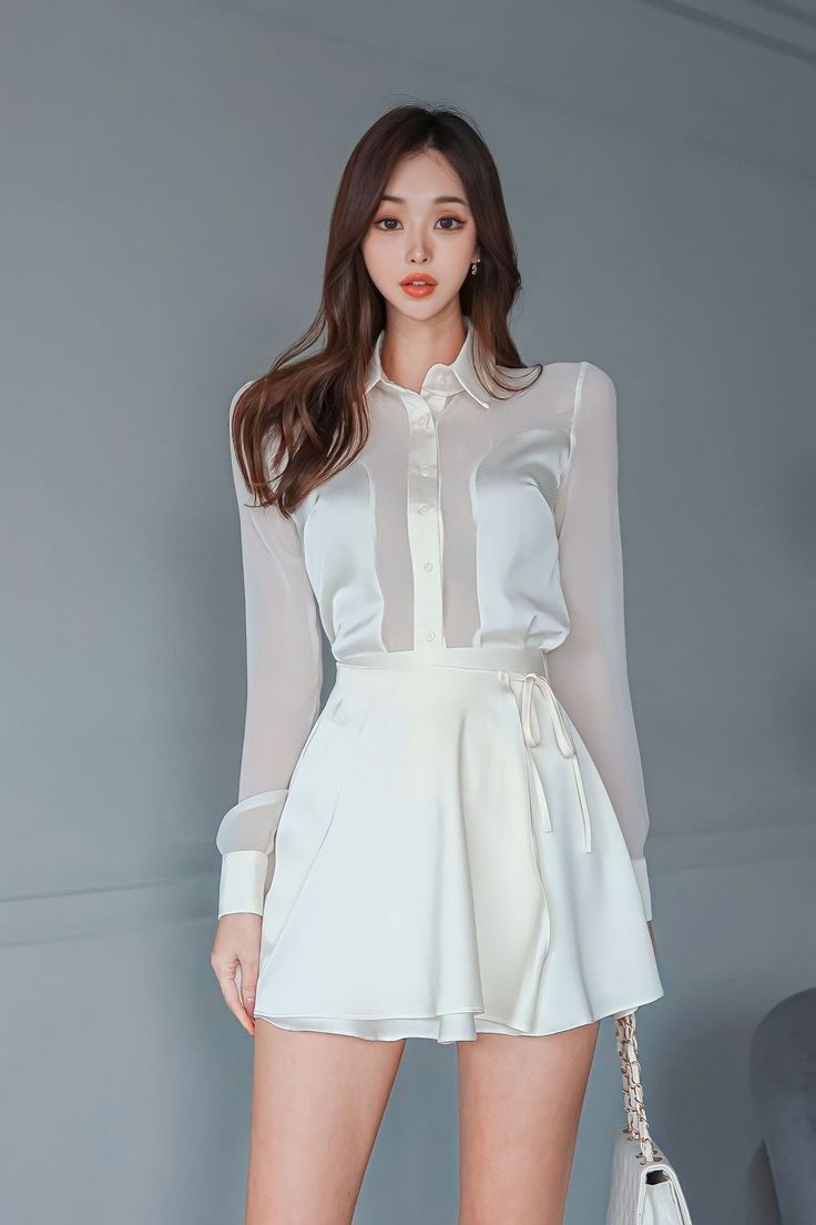 Woman in a white sheer shirt and mini skirt against a gray background