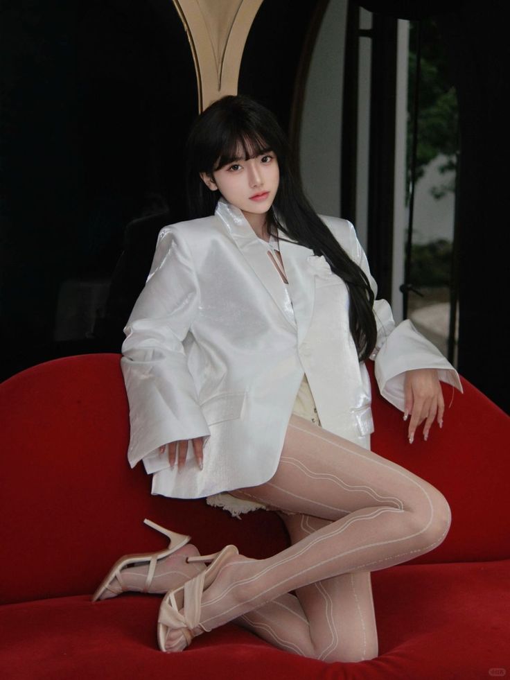 Woman in a white blazer and sheer stockings posing on a red couch