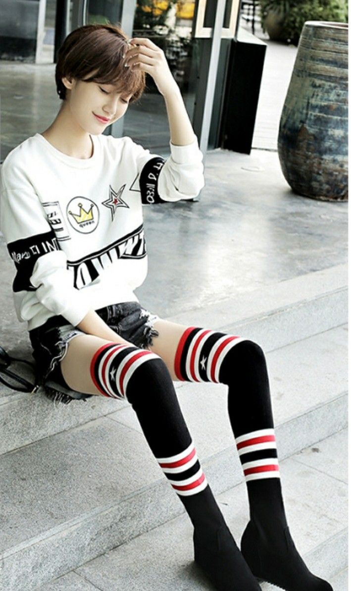 Woman with short hair wearing a white sweatshirt, denim shorts, and thigh-high socks