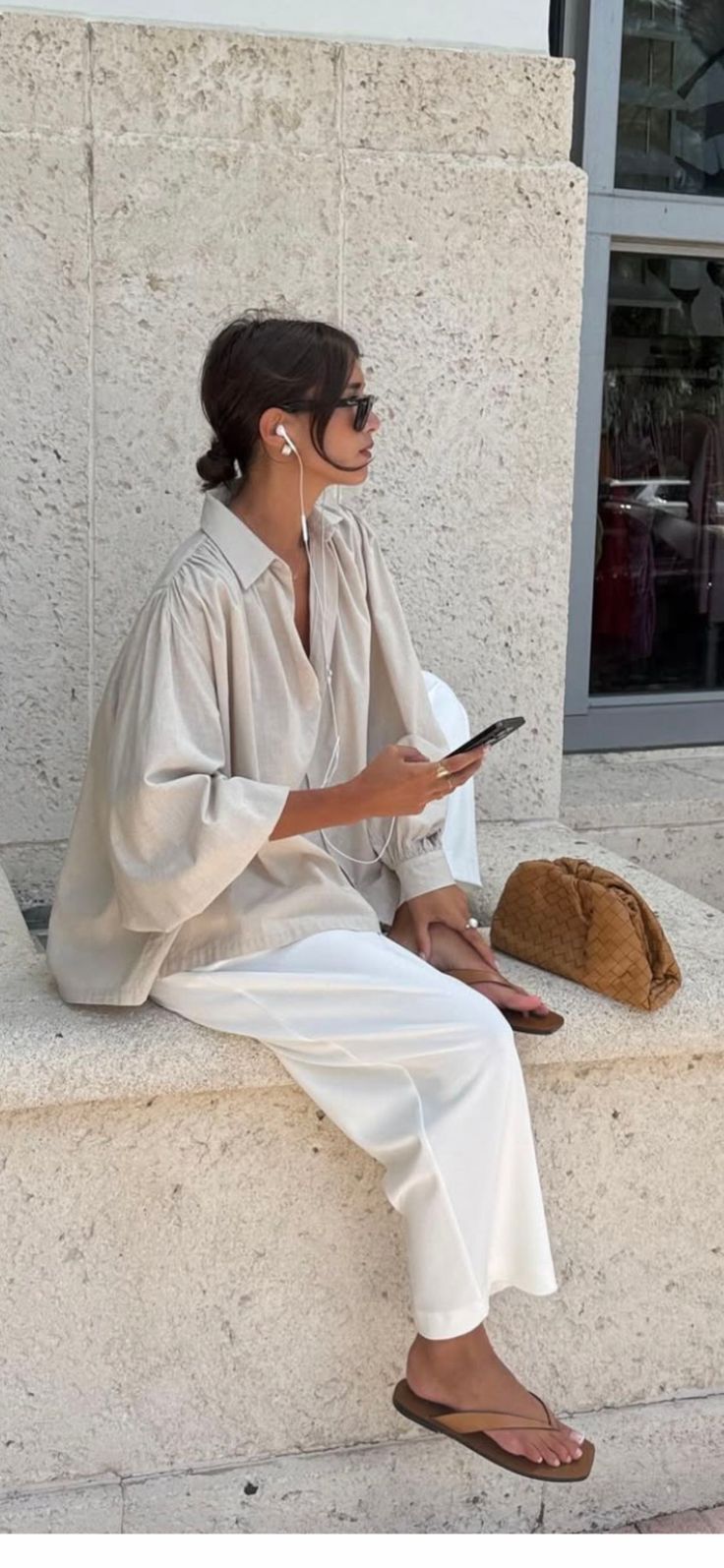 Woman with bun hair, sunglasses, and earbuds sitting outdoors