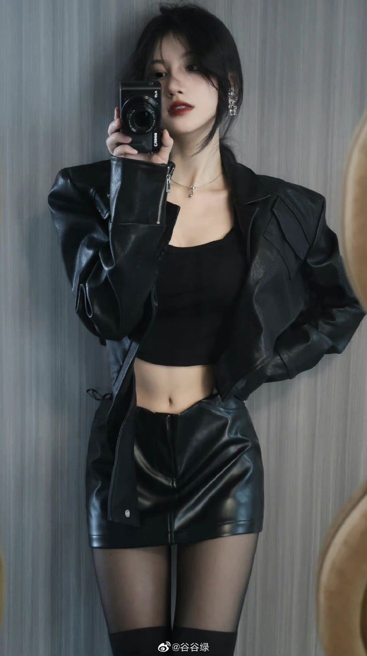 Woman in a black leather jacket and mini skirt taking a mirror selfie
