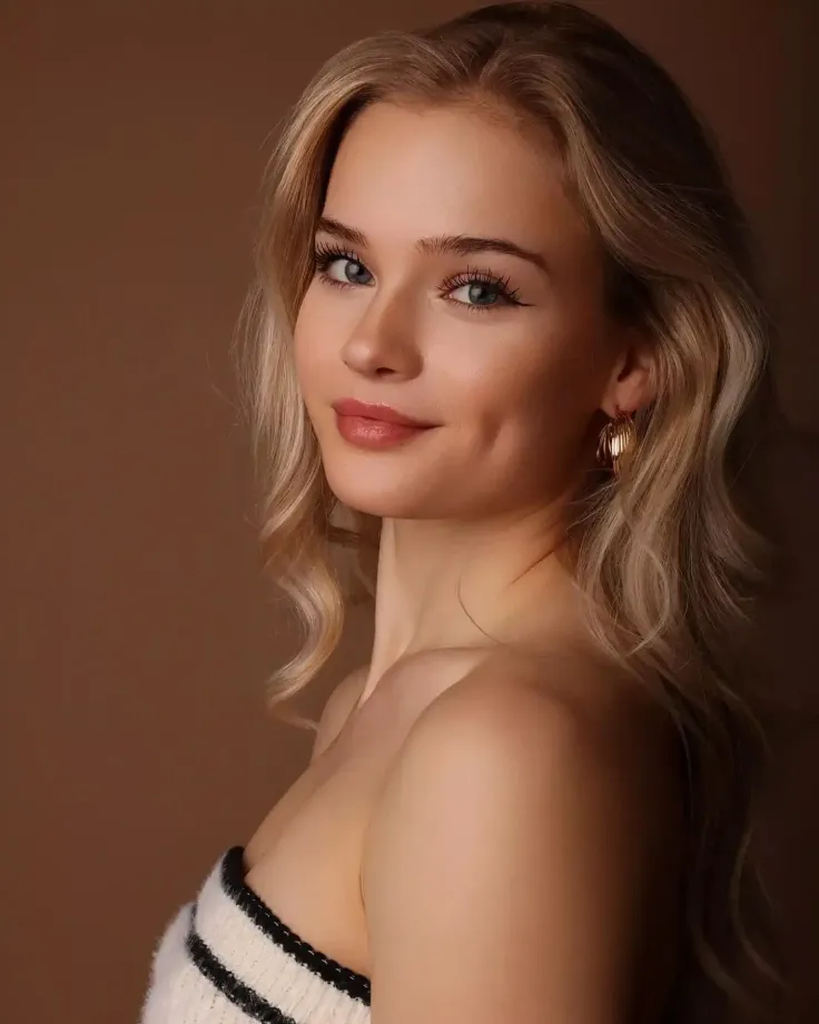 Blonde woman with wavy hair and gold earrings against a brown background