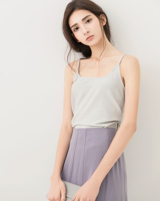 Woman with long hair wearing a silver top and purple skirt, holding a clutch bag