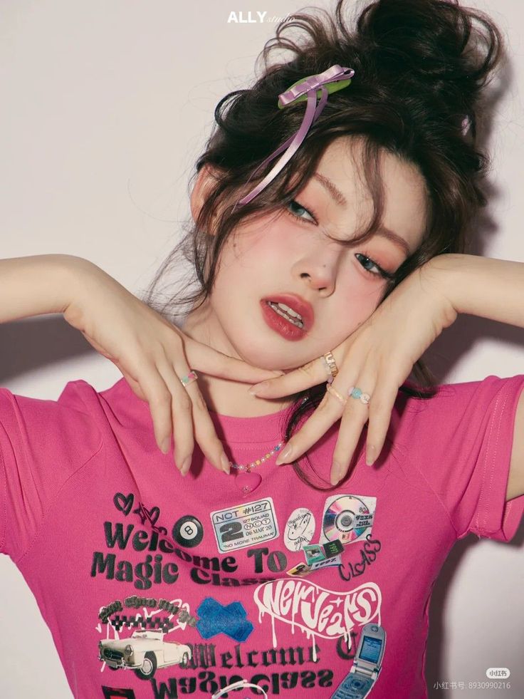 Woman in a pink graphic t-shirt with a messy bun and colorful makeup