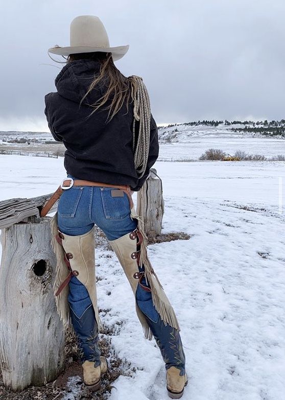 Person in cowboy hat and chaps looking out at a snowy field