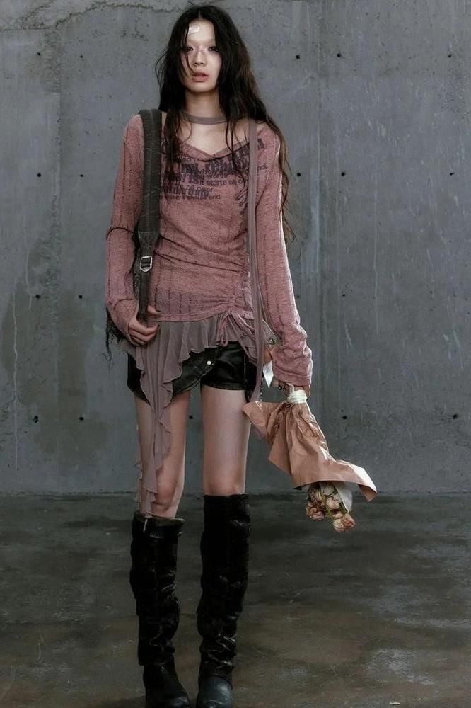 Woman with long black hair wearing leather shorts and black boots against a concrete wall